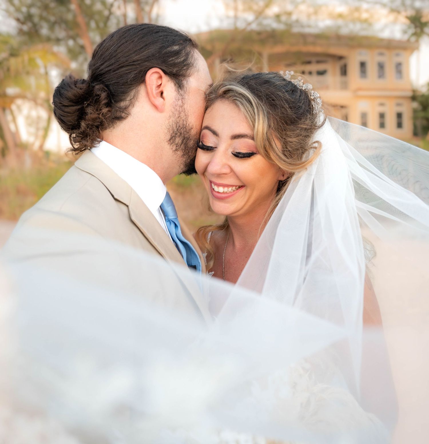 Tender moment shared under flowing white veil with soft natural lighting.