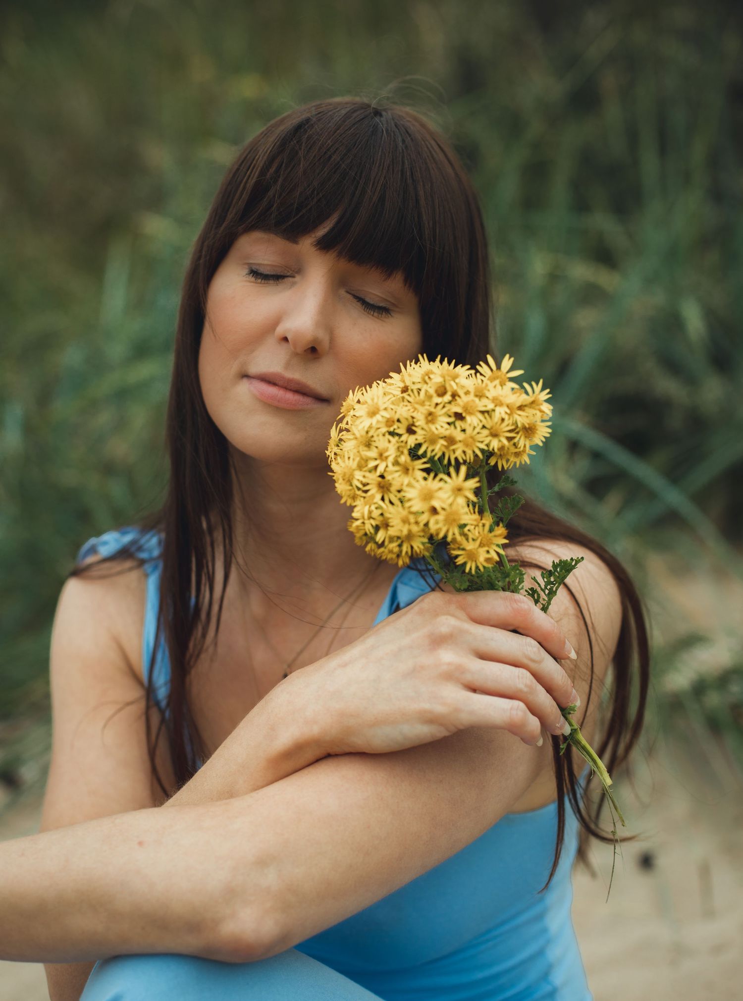 Person in blue tank top holding yellow wildflowers in a dreamy outdoor setting.
