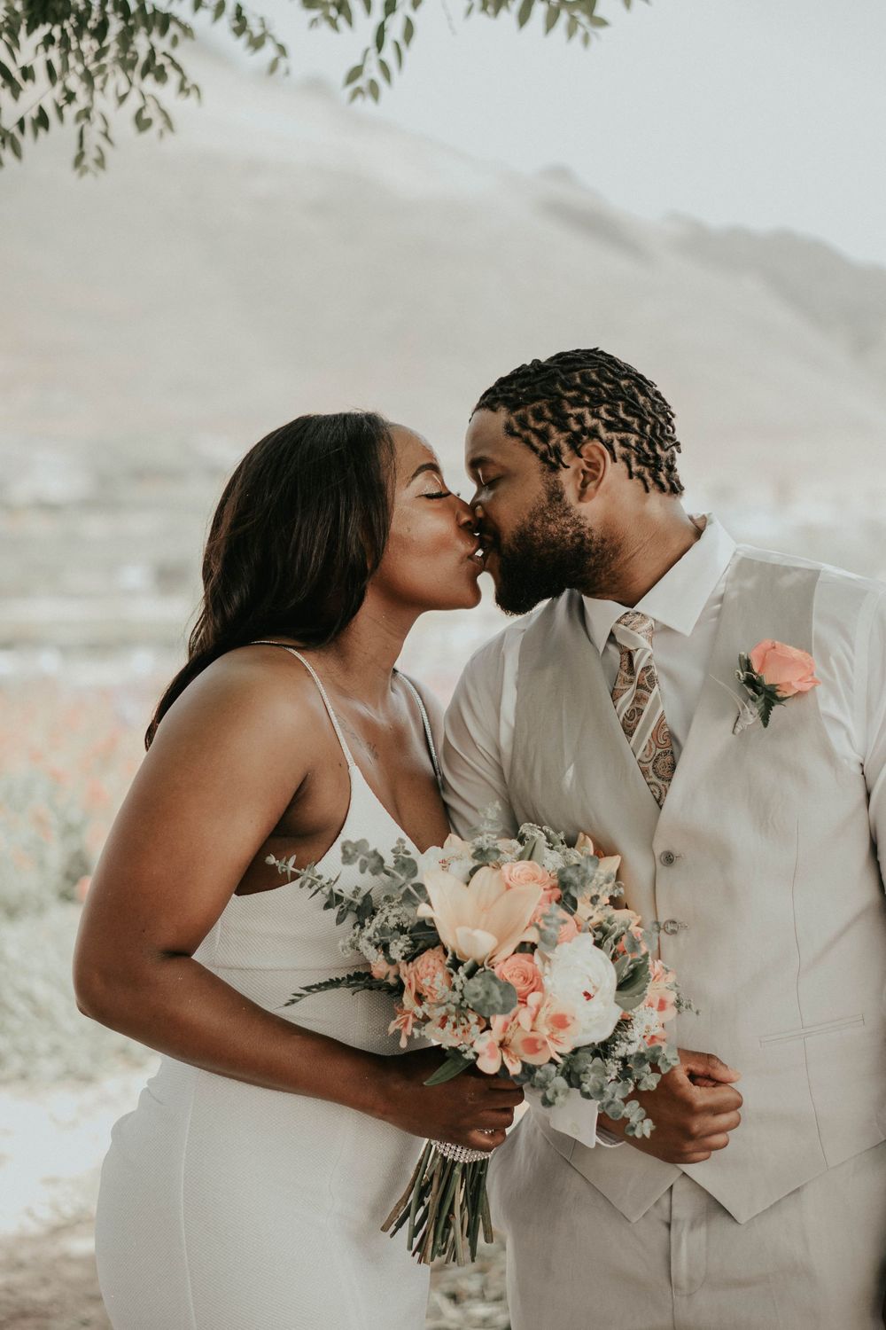 Bride and groom sharing intimate moment with floral bouquet in outdoor setting.