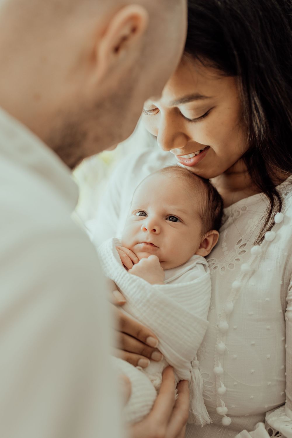 Tender family moment with newborn baby wrapped in white swaddle.