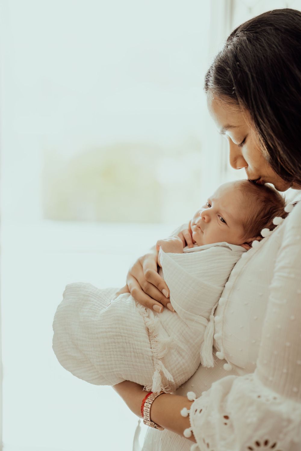 Intimate moment between parent and newborn baby wrapped in white swaddle.