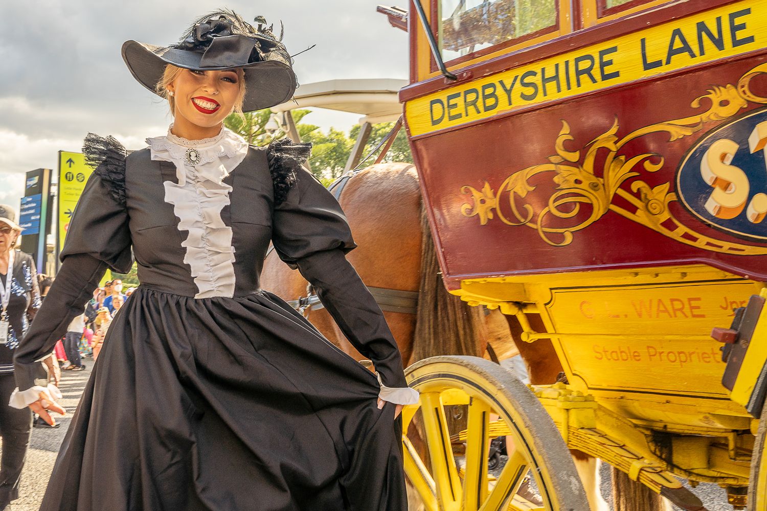 Woman in Victorian black dress posing beside a vintage Derbyshire Lane horse-drawn stagecoach.