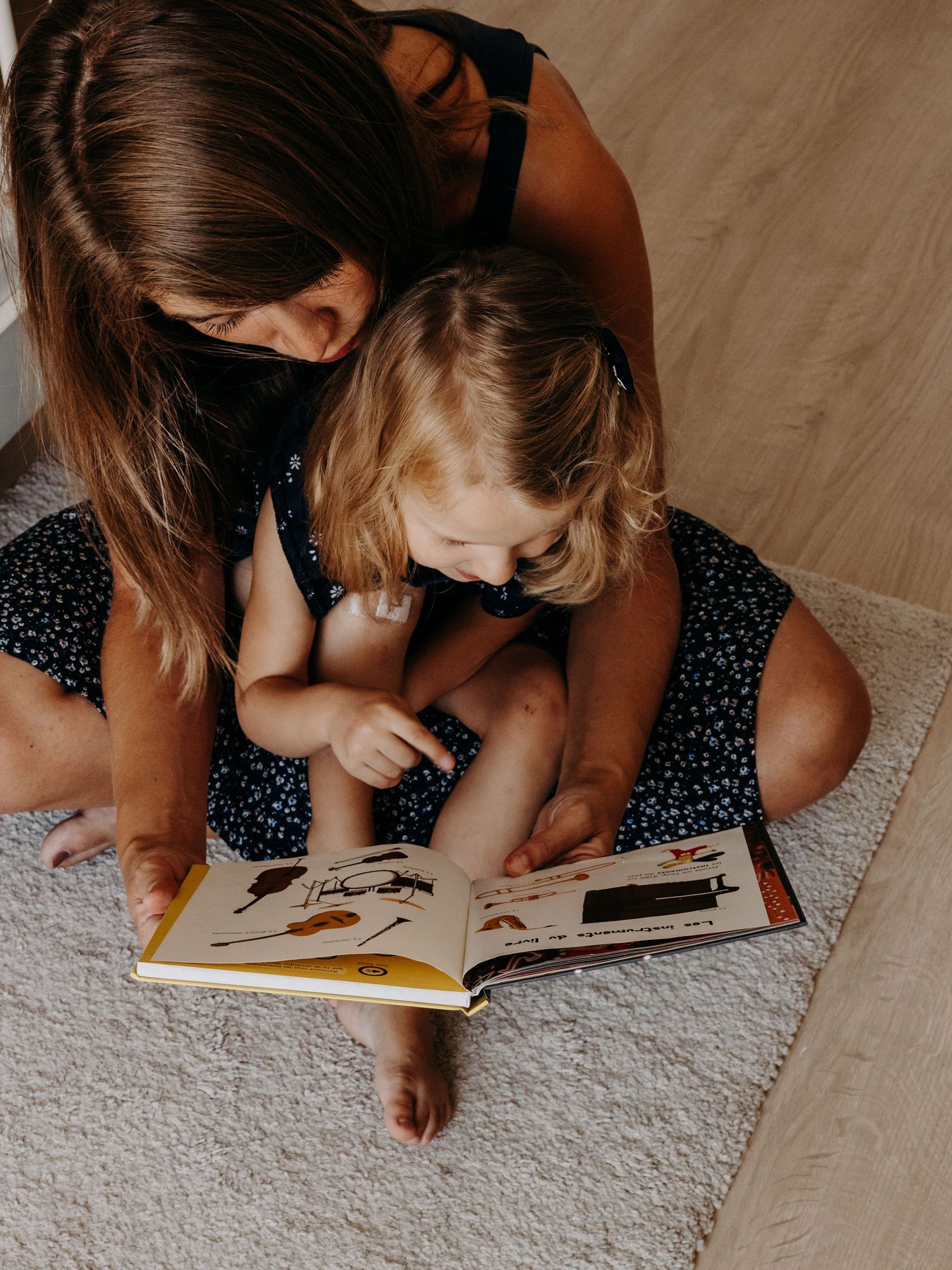 A parent and child share a moment reading a picture book together on a carpeted floor.
