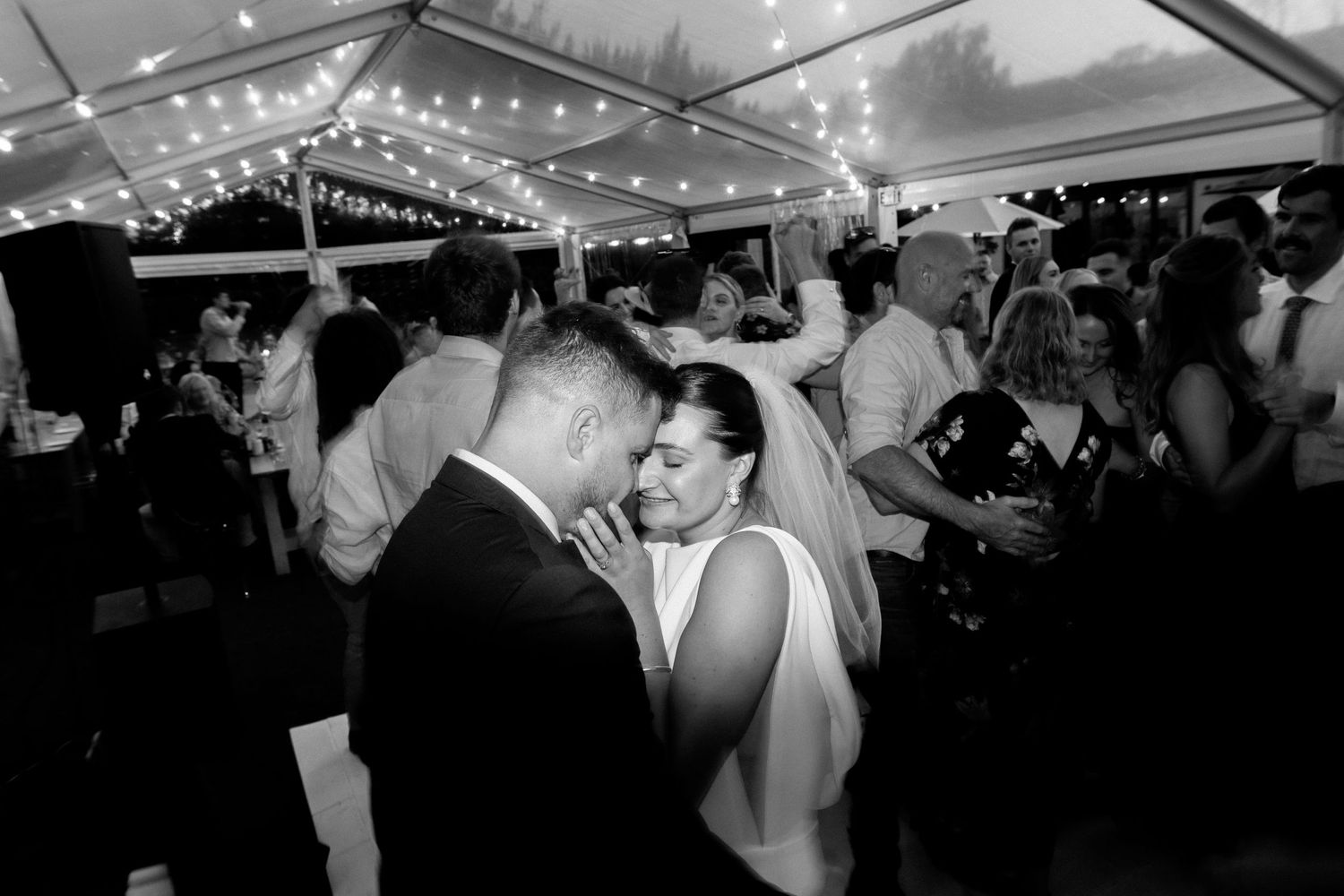 Romantic black and white dance scene under tent with string lights.