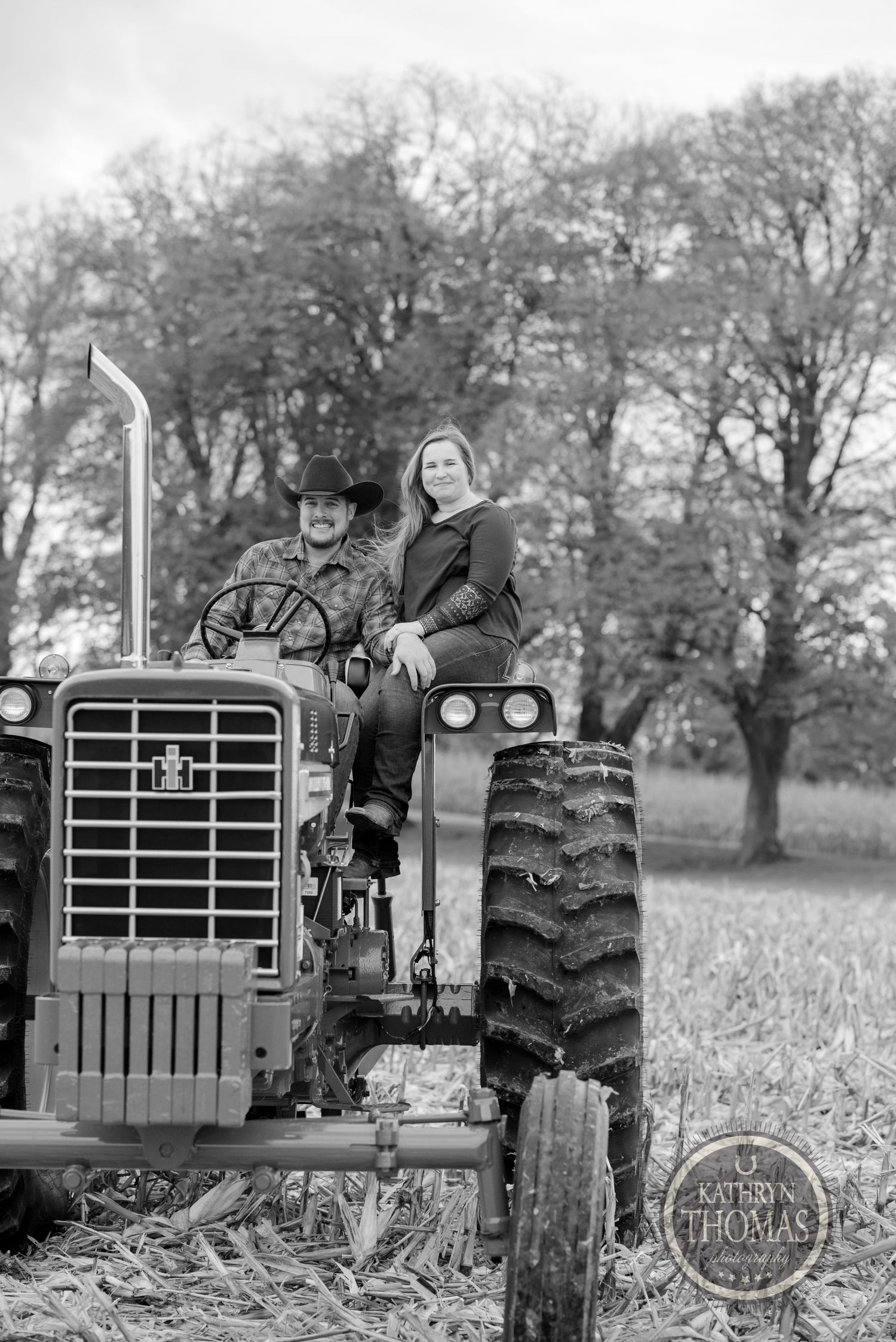A vintage black and white photo of a person sitting on a farm tractor in a rural setting.