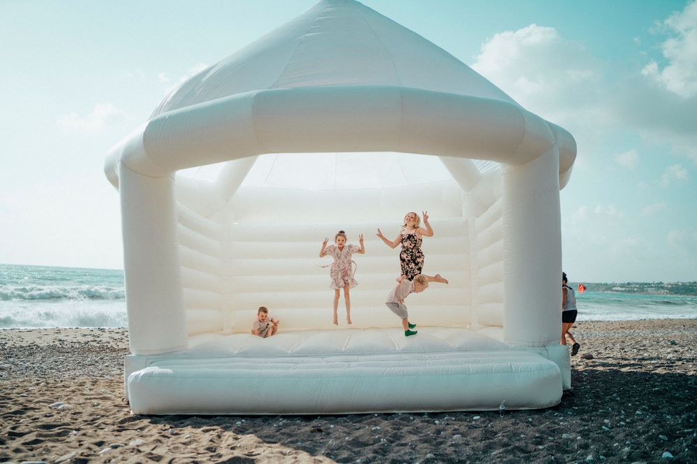 People jumping and playing inside a white inflatable bounce house on a sunny beach.