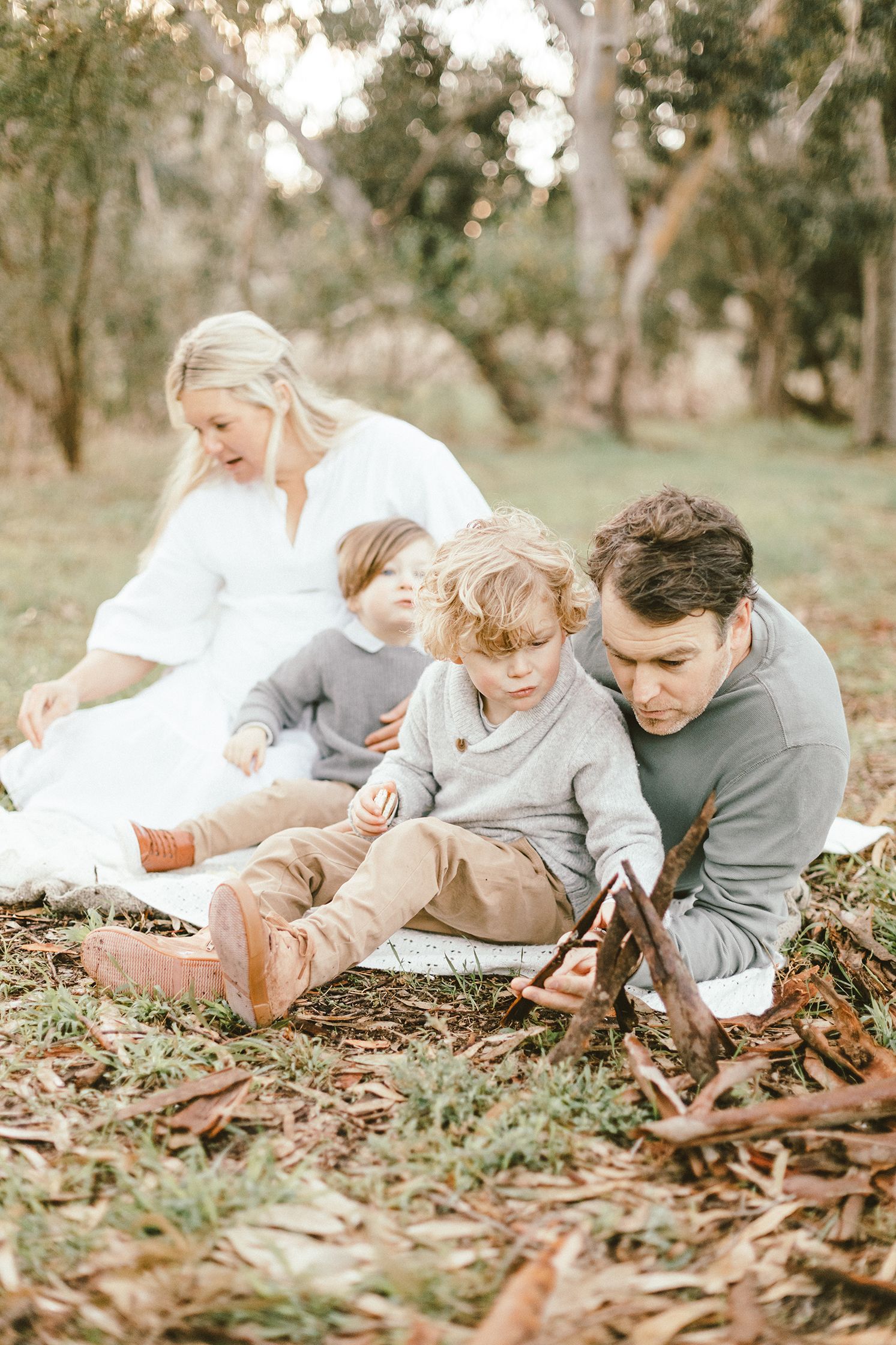 Family sitting together on fallen leaves in a wooded setting during autumn.