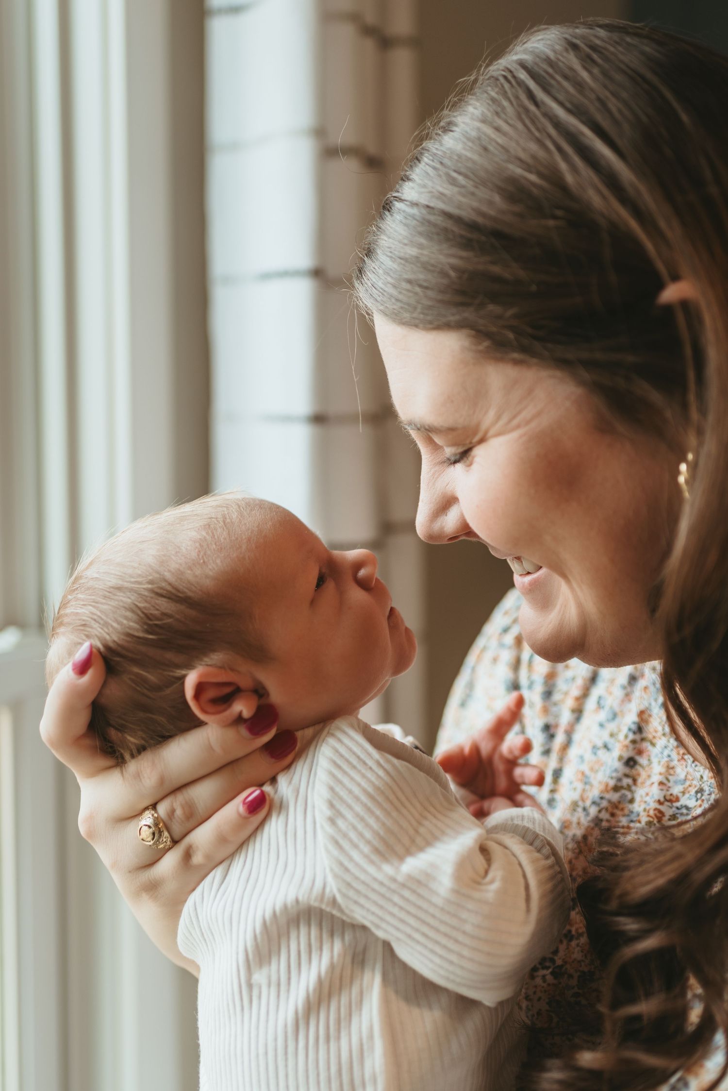Tender moment between parent and newborn baby by window in warm light.
