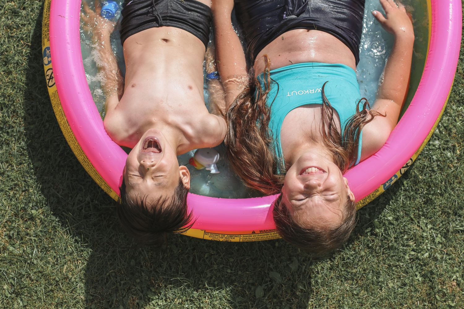 Outdoor summer photoshoot with cousins lying in a paddling pool in the garden.