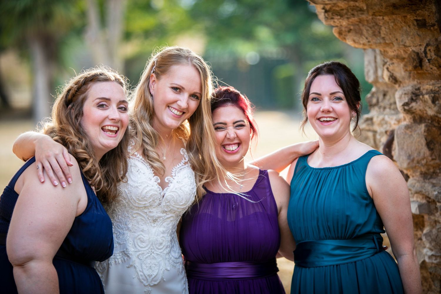 A group poses together wearing elegant navy and purple bridesmaid dresses under a stone archway.