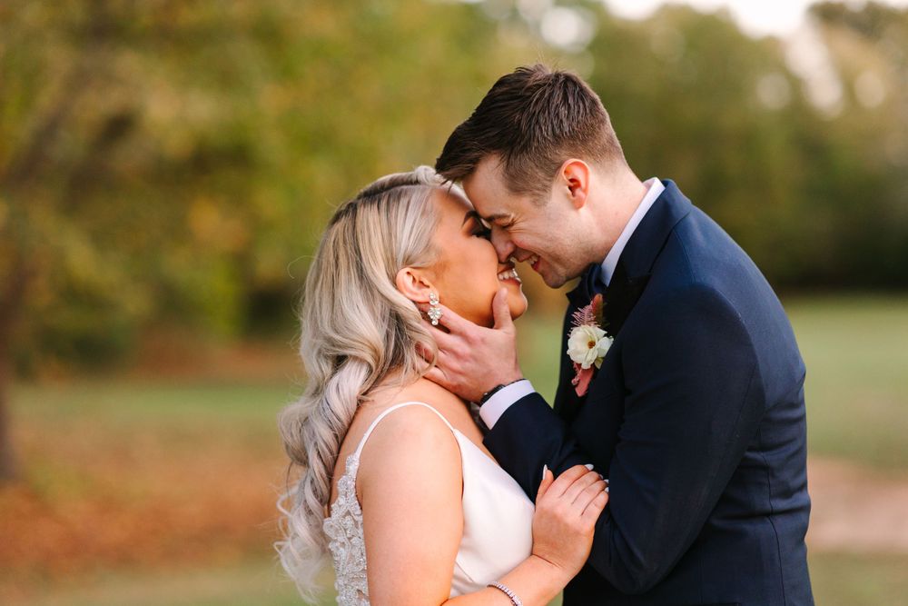 A close-up romantic moment captured outdoors during golden hour with fall foliage in background.