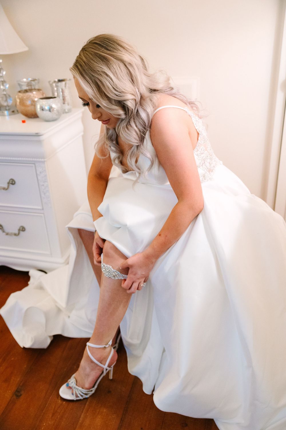 Close up of bride adjusting garter on leg while wearing white wedding dress.