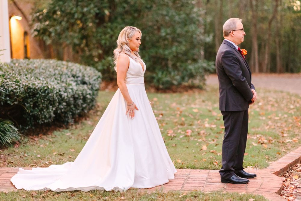 A pre-ceremony first look moment on a brick pathway surrounded by autumn foliage.