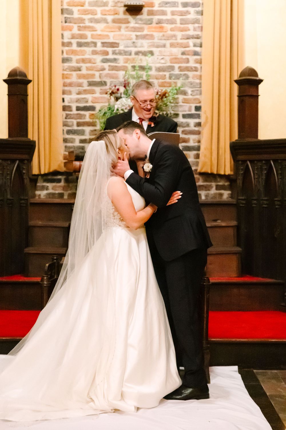 A romantic wedding ceremony moment beneath a decorative cross in a traditional church setting.