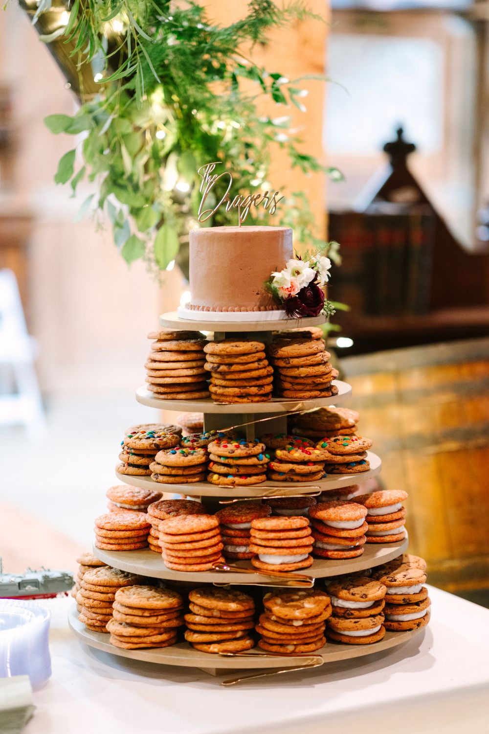 Tiered display of chocolate chip cookies topped with a small cake and greenery.