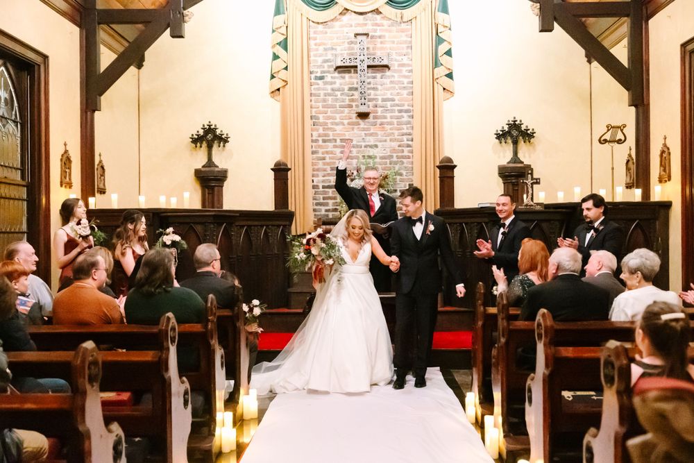 A joyous wedding celebration with guests applauding in a traditional chapel with wooden pews.