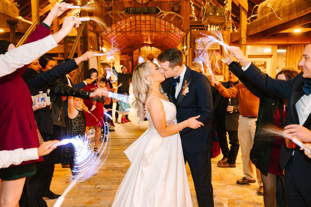 Newlyweds share a kiss under sparklers held by guests during their rustic barn reception exit.