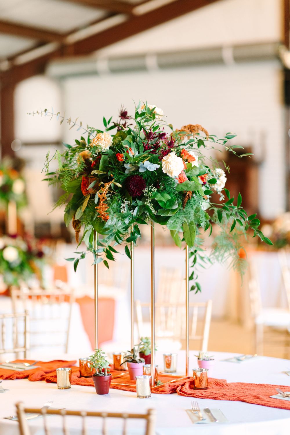 Elevated floral centerpiece with greenery and white flowers on wedding reception table.