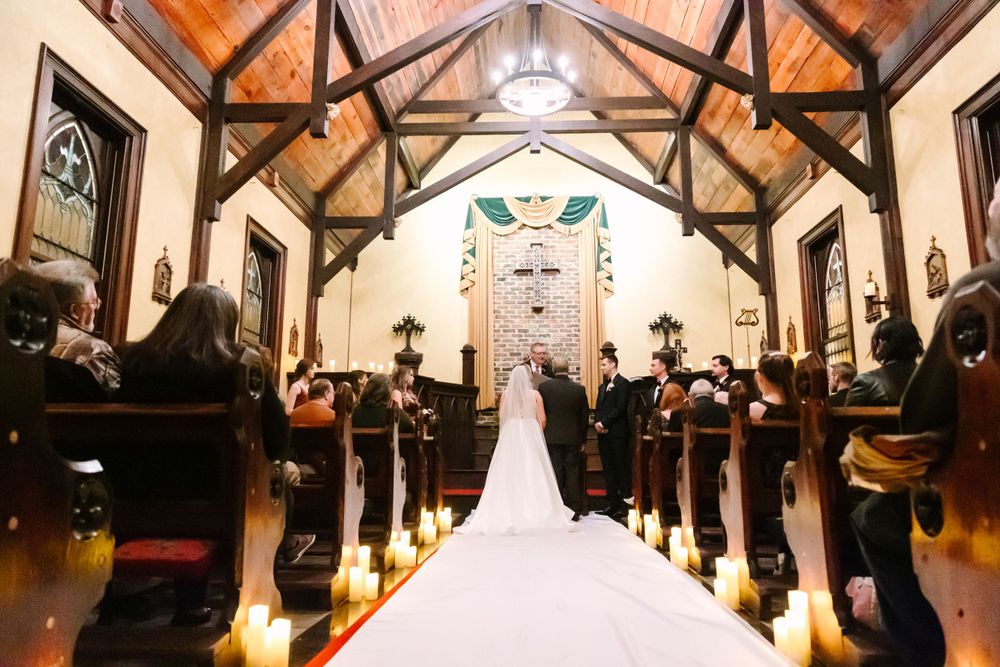 Church wedding ceremony from back of aisle with candles and wooden beam ceiling.