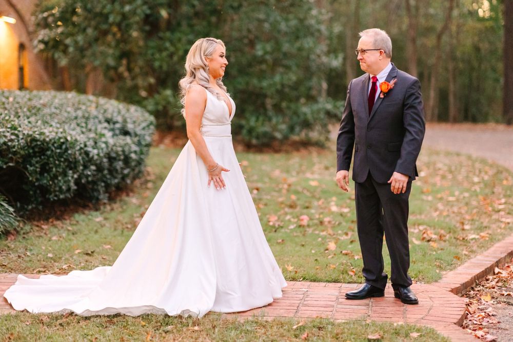 A bride in a flowing white gown and groom in dark suit share a first look moment outdoors.