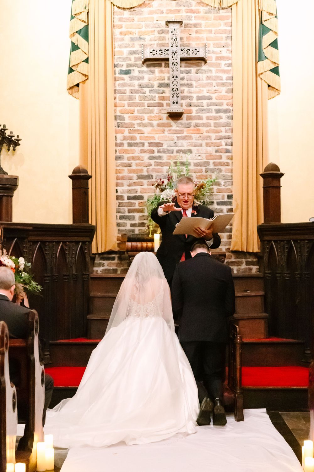 A wedding ceremony in progress with a white aisle runner and red carpet in a historic chapel.