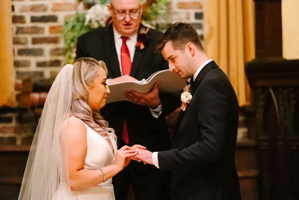 A ring exchange ceremony in a traditional church setting with exposed brick walls.