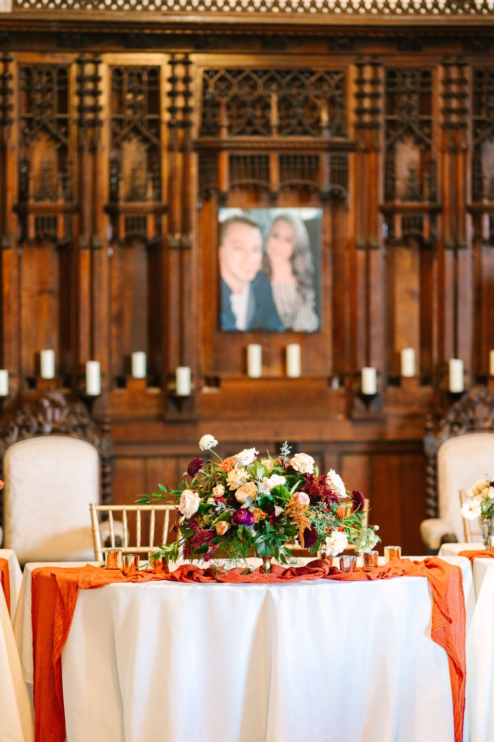 Wedding reception table with orange accents and floral arrangement against ornate wooden backdrop.