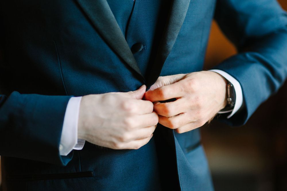 Close-up of hands buttoning a navy blue suit jacket.