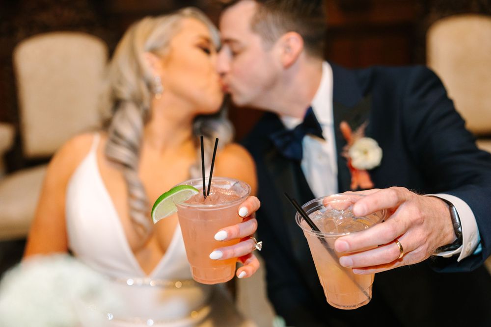 Couple shares romantic moment while holding cocktails at wedding reception.