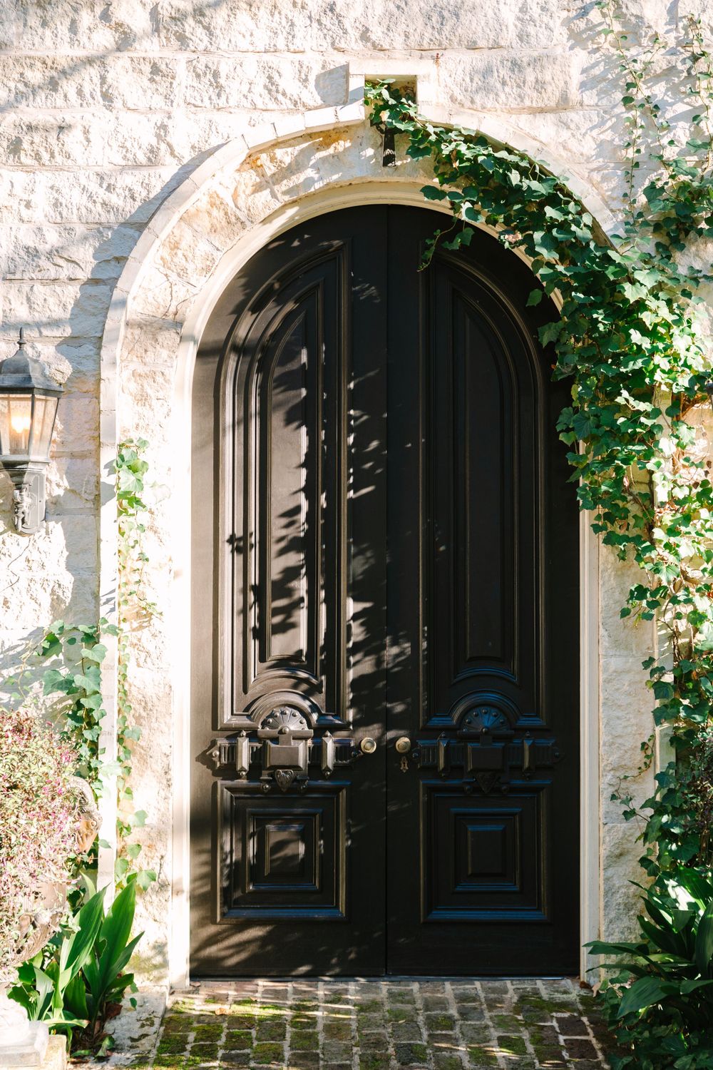 Elegant black arched door with ivy growing around stone entrance.