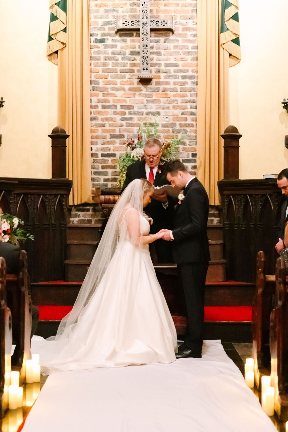 A wedding ceremony in progress at a charming brick chapel with candles lining the aisle.