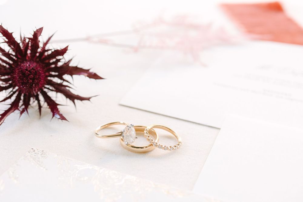 Three gold wedding rings arranged on white surface with burgundy flower accent.