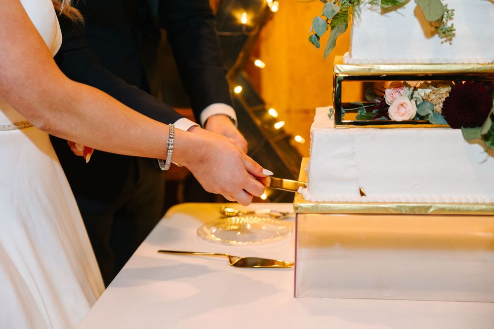 Close-up of hands cutting wedding cake with elegant gold decor.