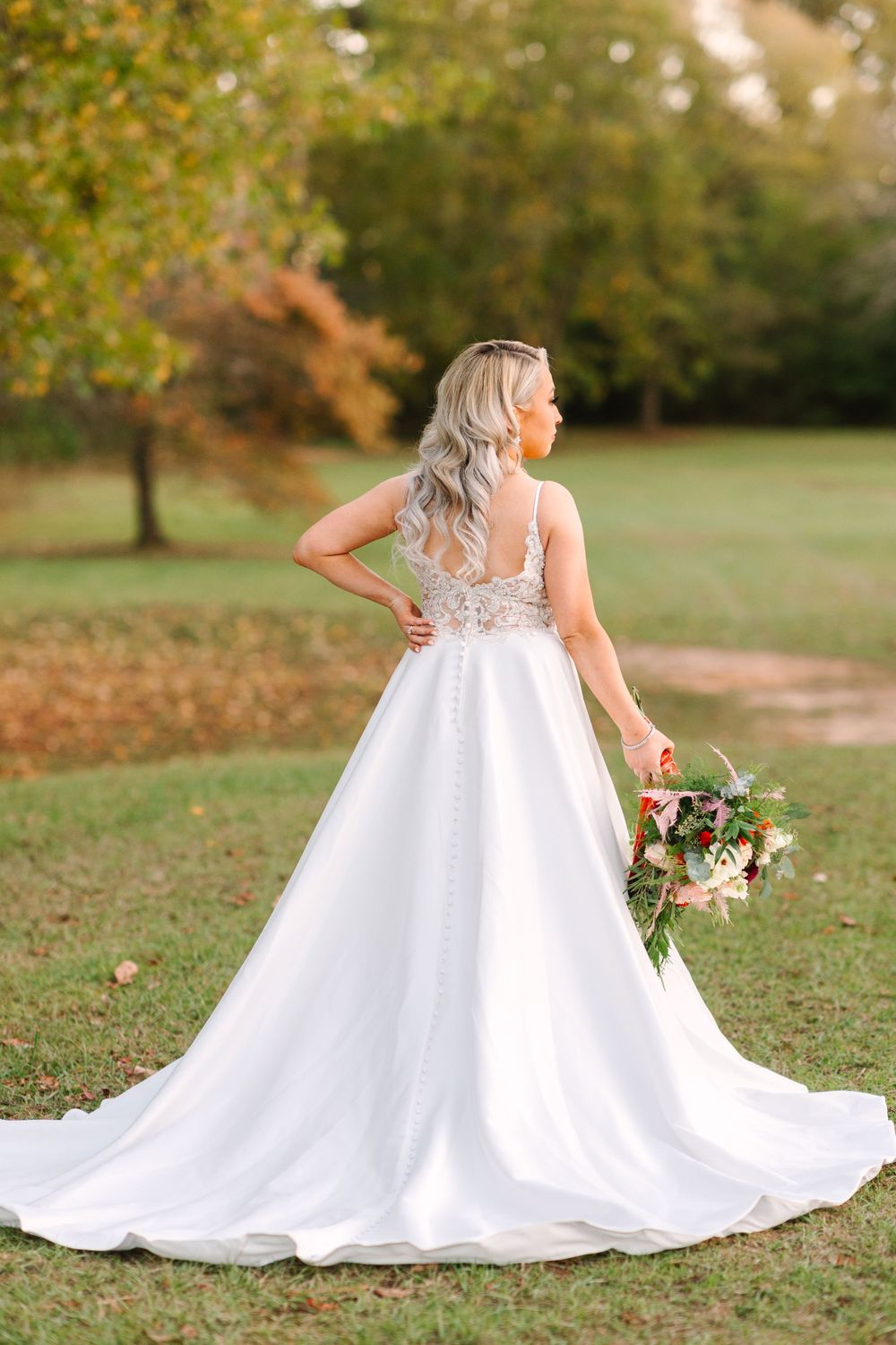 A stunning white wedding dress with lace details and long train captured during a fall outdoor photo session.