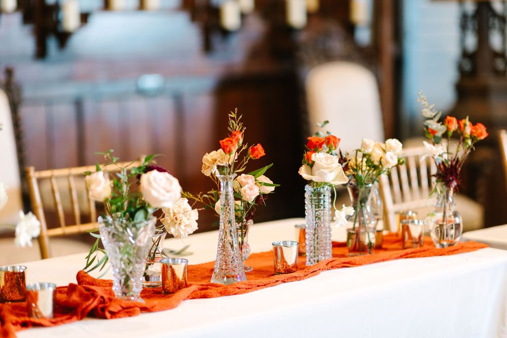 Wedding reception table decorated with glass bud vases and orange table runner.