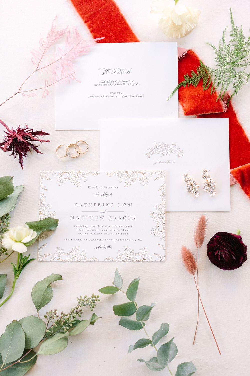 Elegant wedding invitation suite with gold rings and red floral accents on white background.