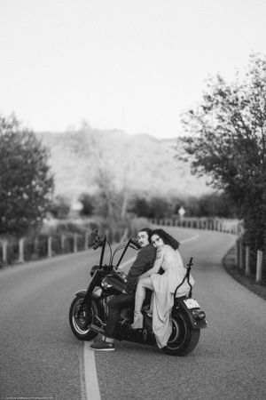 A romantic black and white photo of two people sitting on a motorcycle on a winding road.