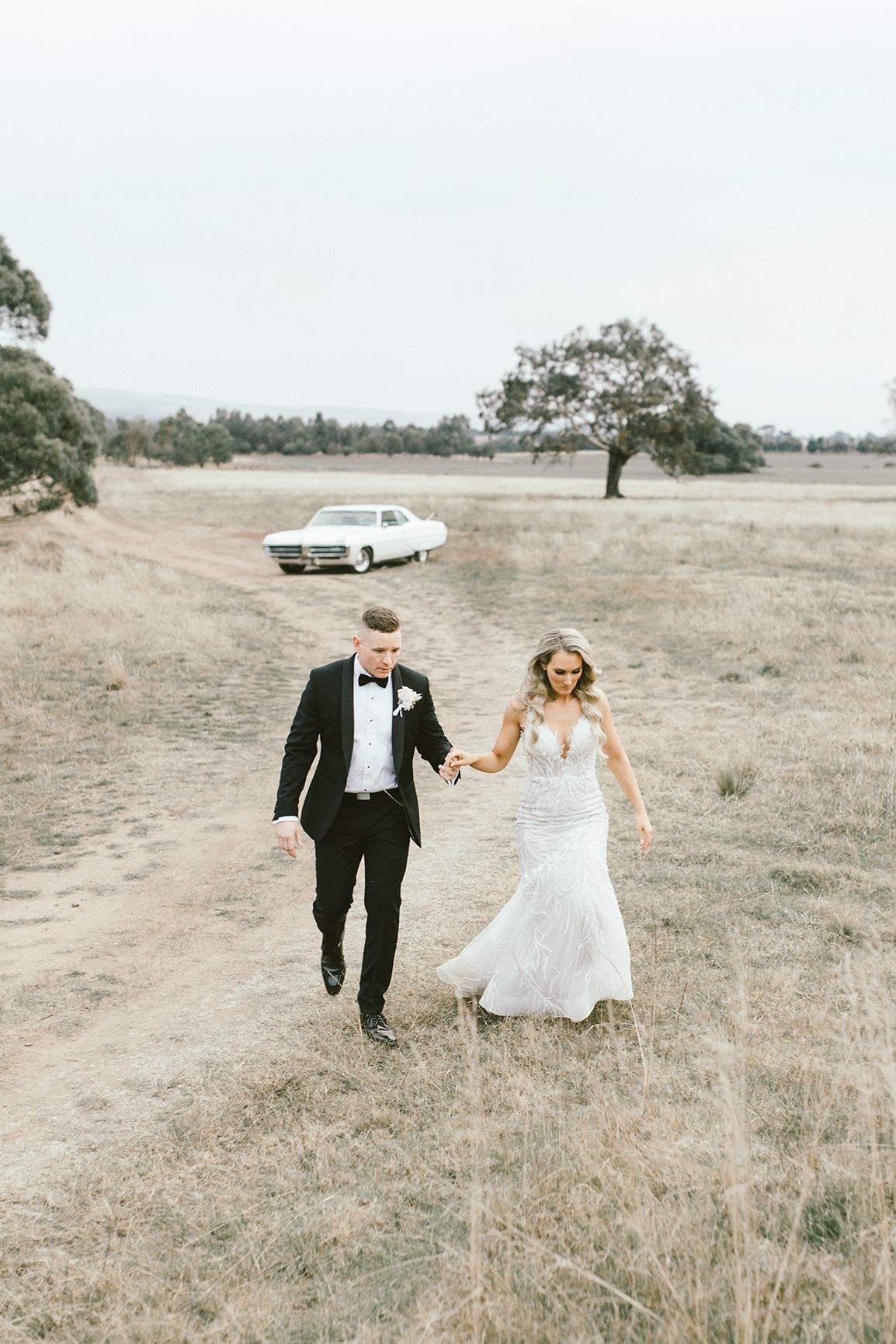 A couple in wedding attire walk through a rustic field together in an artistic photo series.