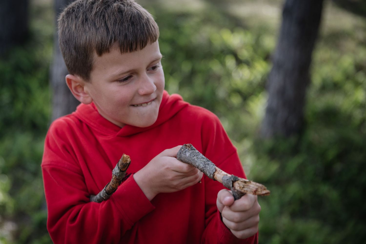 Young person in red sweater examining a small stick in the forest.