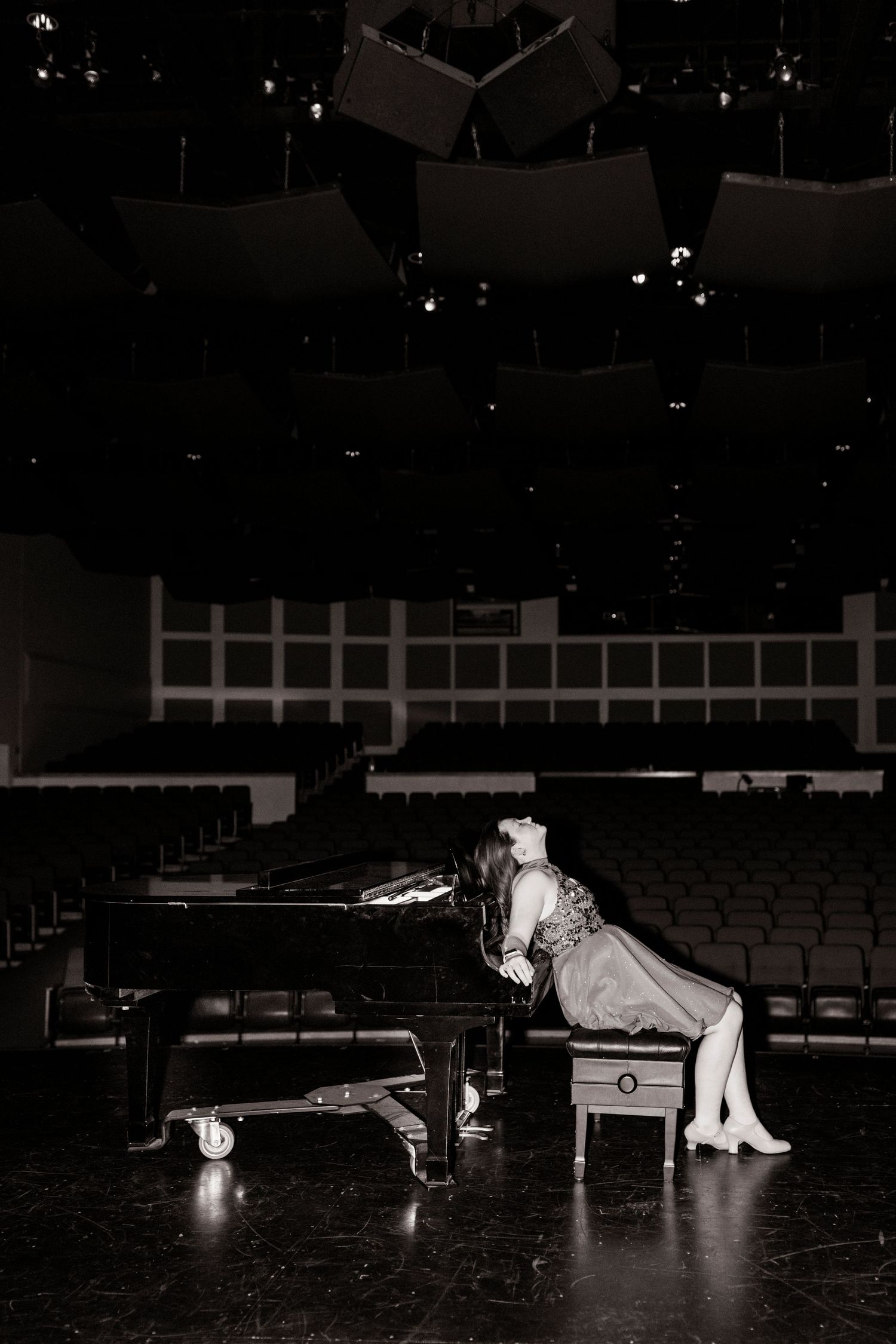 Black and white portrait of young woman leaning on grand piano on theater stage.