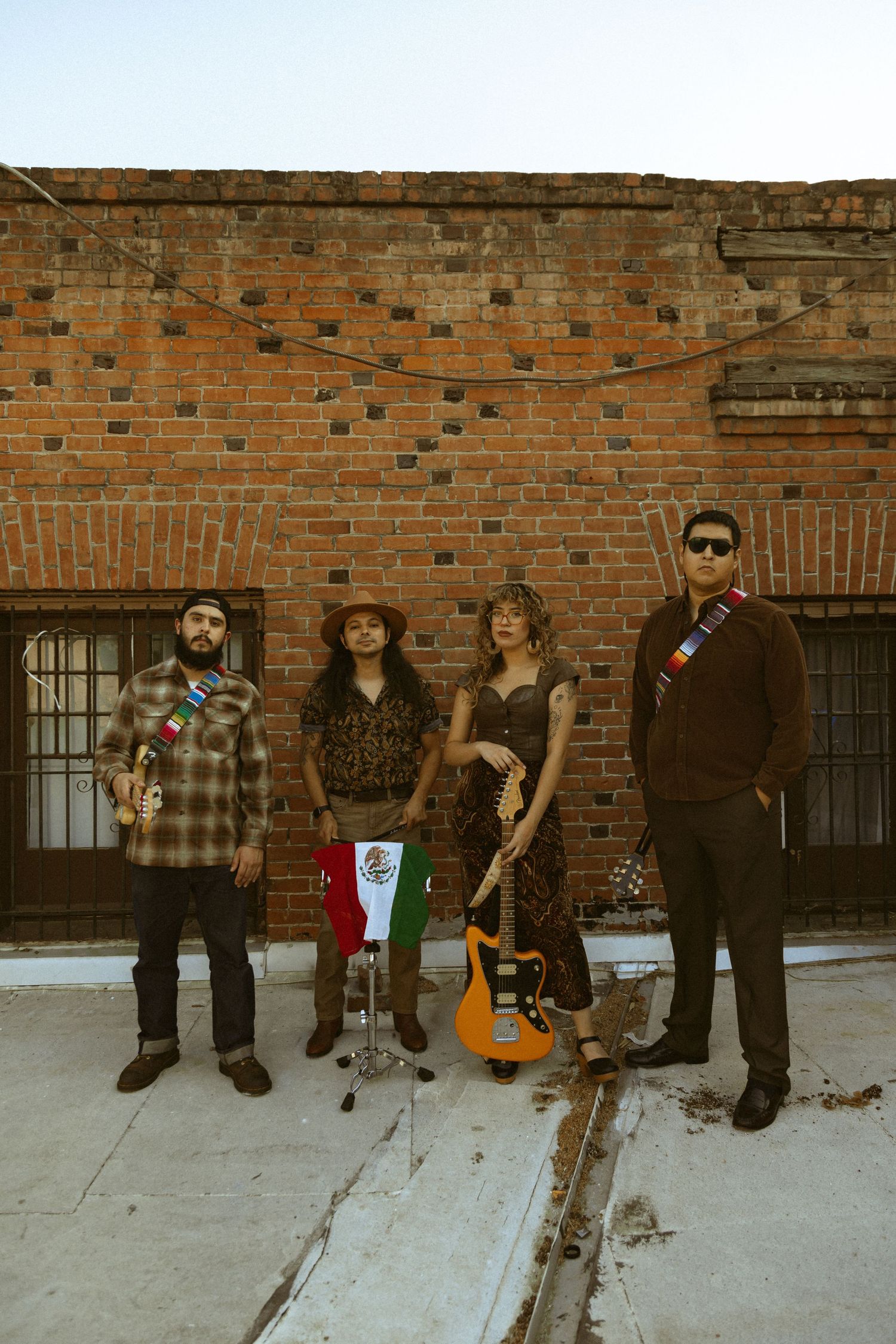 Musicians with instruments pose in front of weathered brick wall.