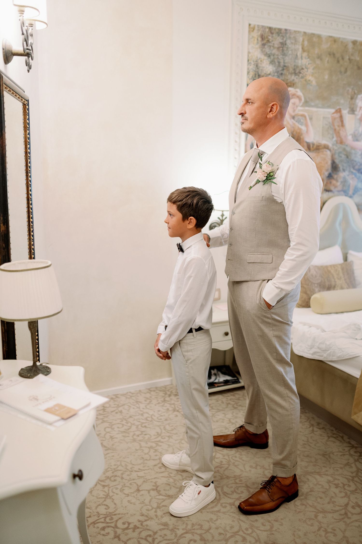 A formal scene showing two people in white and beige attire standing side by side in a room.