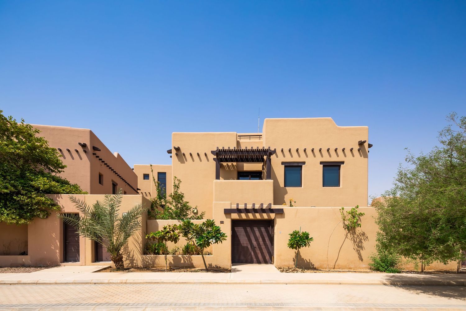 Modern adobe-style desert villa with traditional architectural elements and palm trees under bright blue sky.