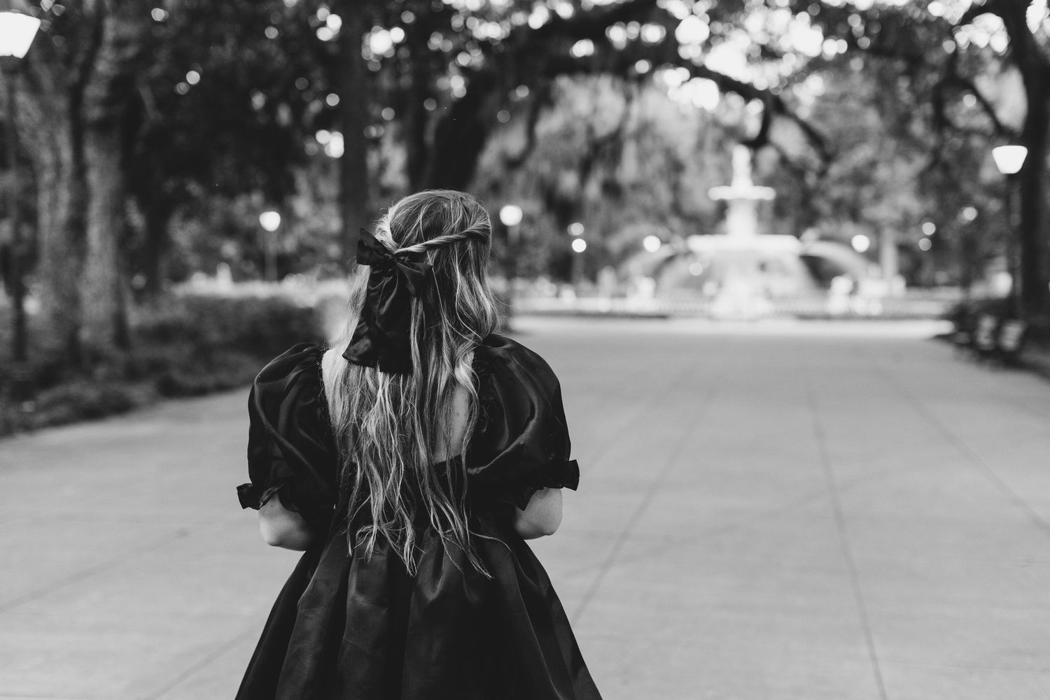 Back view of person with long hair wearing black dress on park pathway.