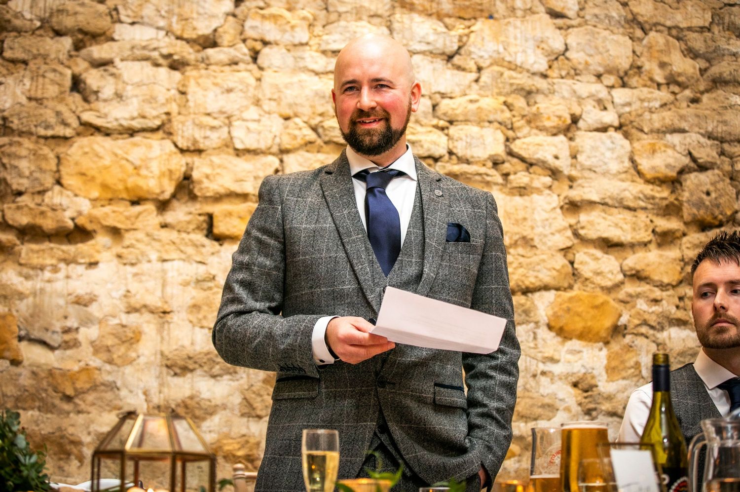 Wedding guests enjoying speeches and toasts at a rustic stone venue.