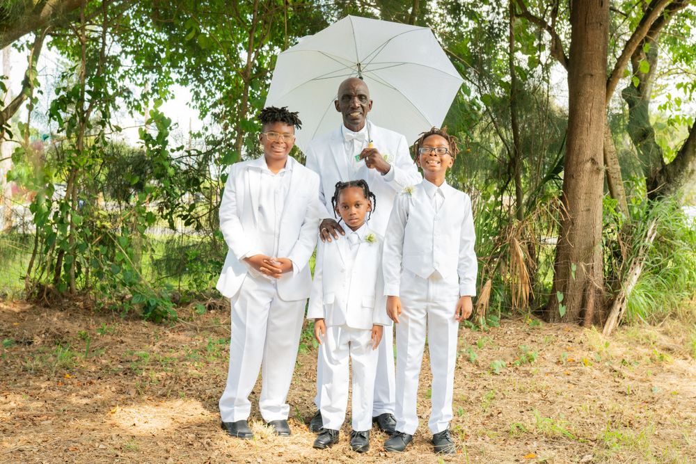 Family dressed in white poses with umbrella in garden setting.