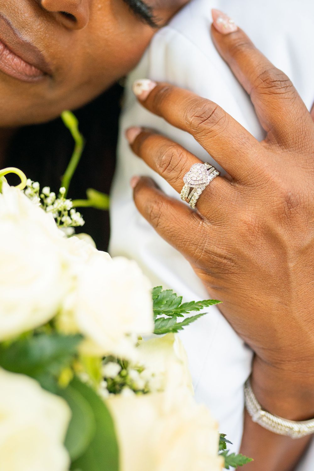 Close-up of elegant diamond engagement ring and white floral bouquet.