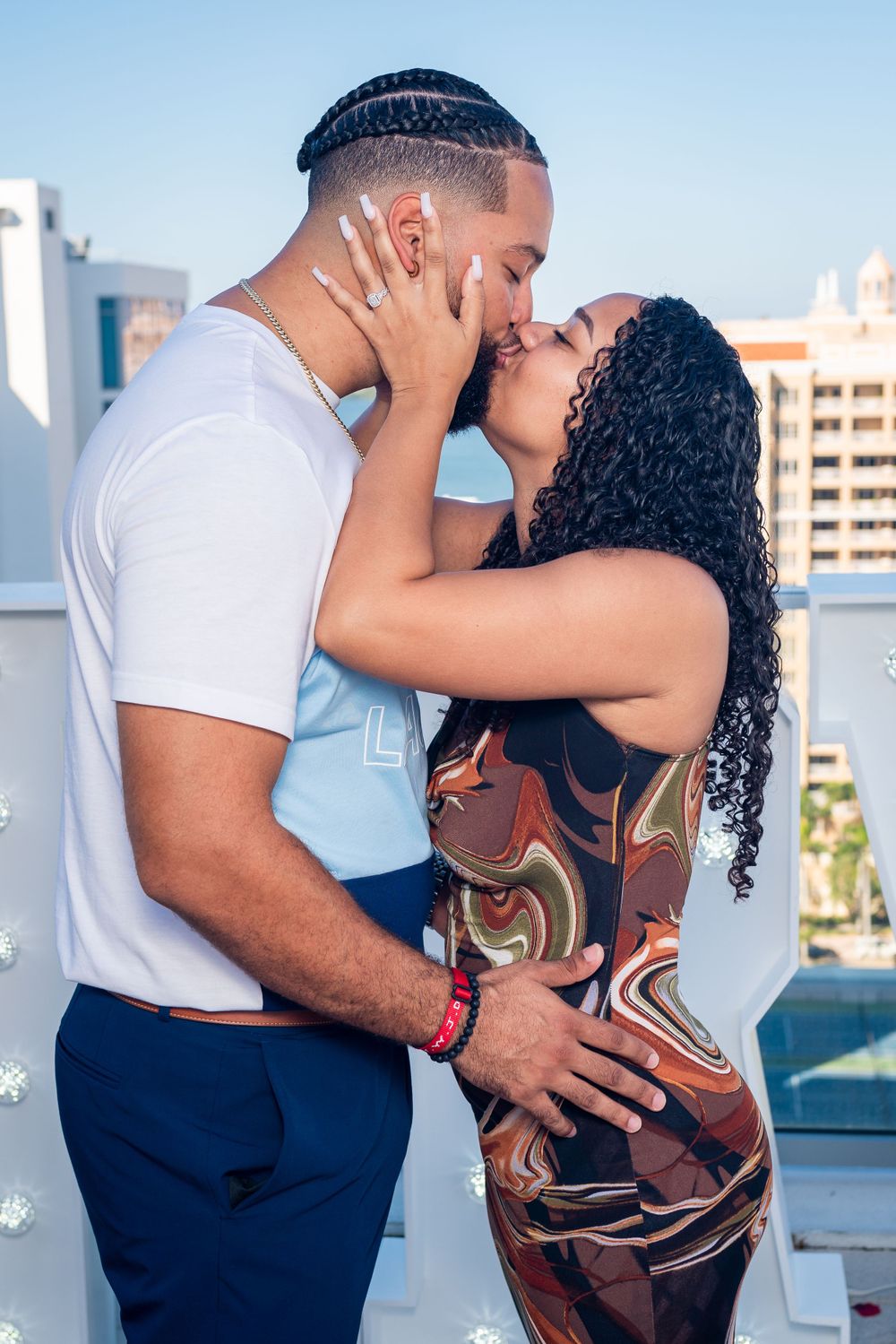 A romantic couple embracing in front of white lettering on an urban rooftop setting.