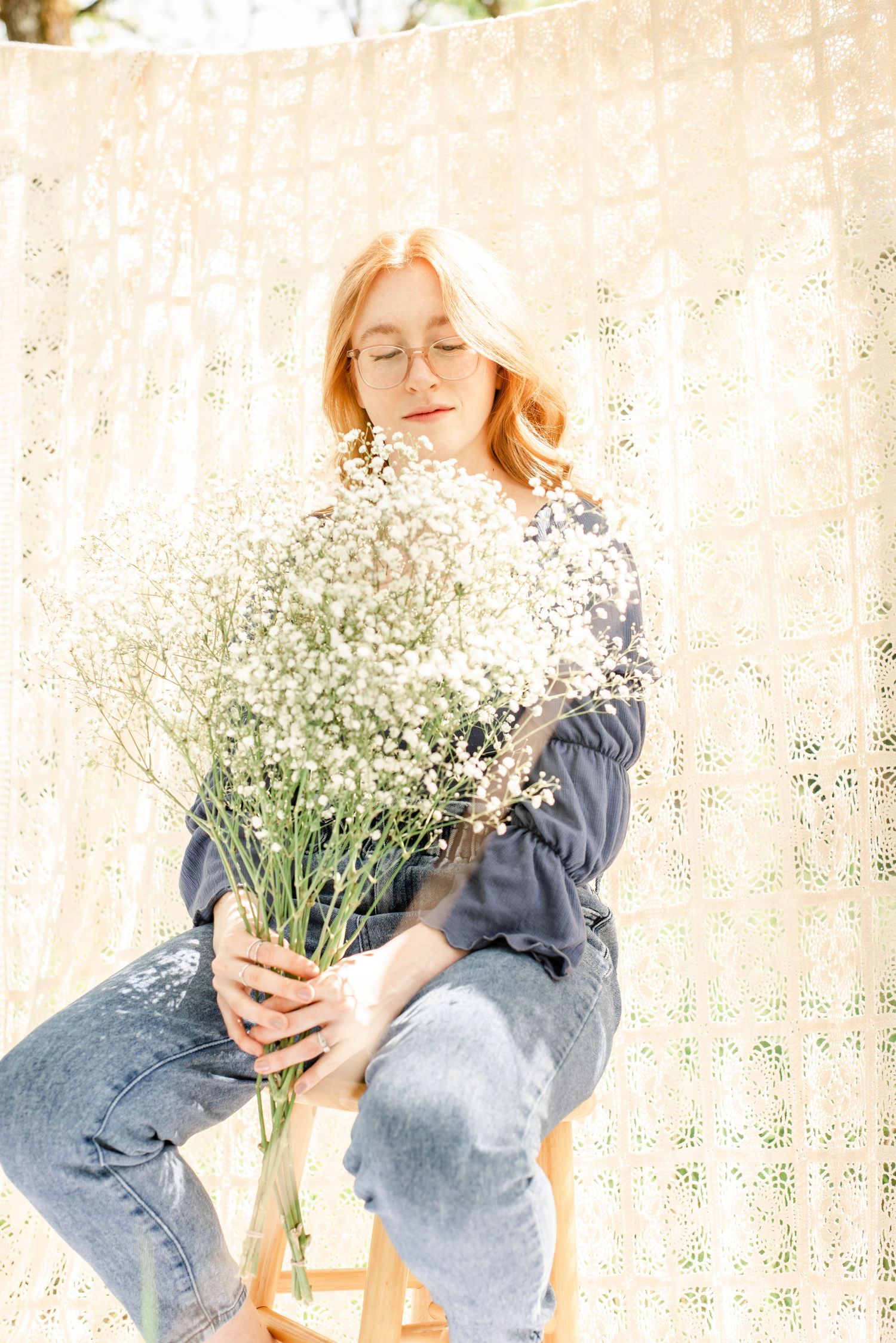 Styled photoshoot featuring white flowers and denim outfit on wooden stool setting.