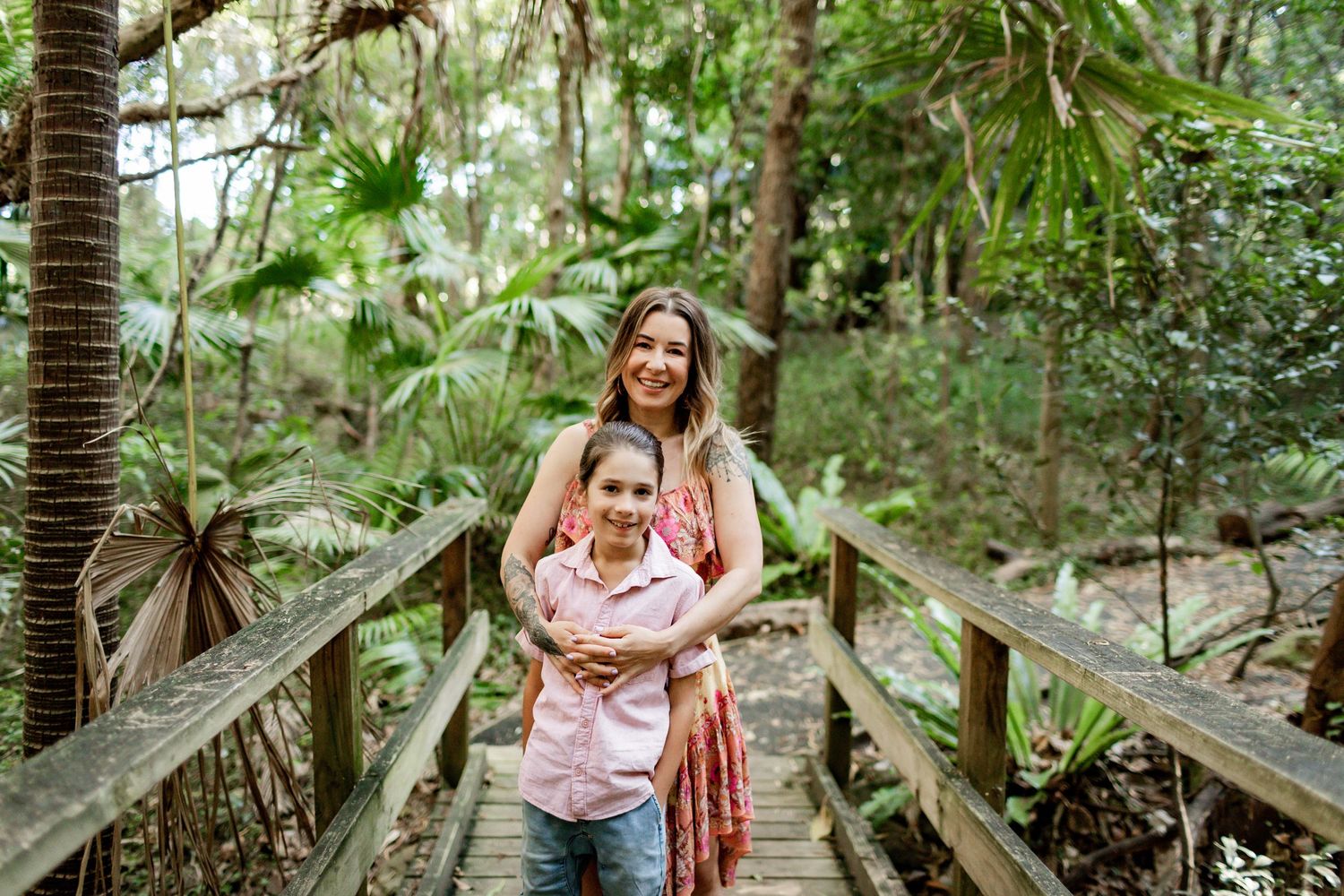 Two people sharing an embrace while standing on a wooden bridge in a lush forest setting.